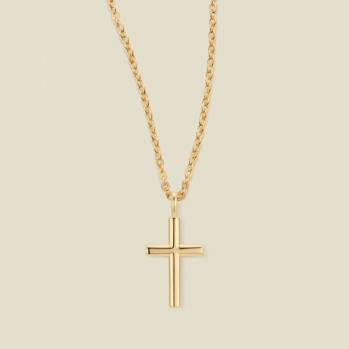 A gold cross pendant necklace on a delicate gold chain, centered against a solid light beige background.
