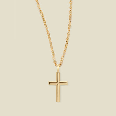 A gold cross pendant necklace on a delicate gold chain, centered against a solid light beige background.