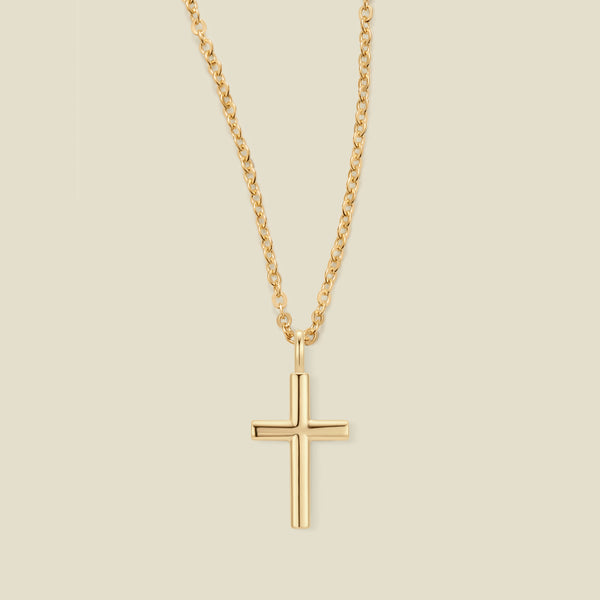 A gold cross pendant necklace on a delicate gold chain, centered against a solid light beige background.