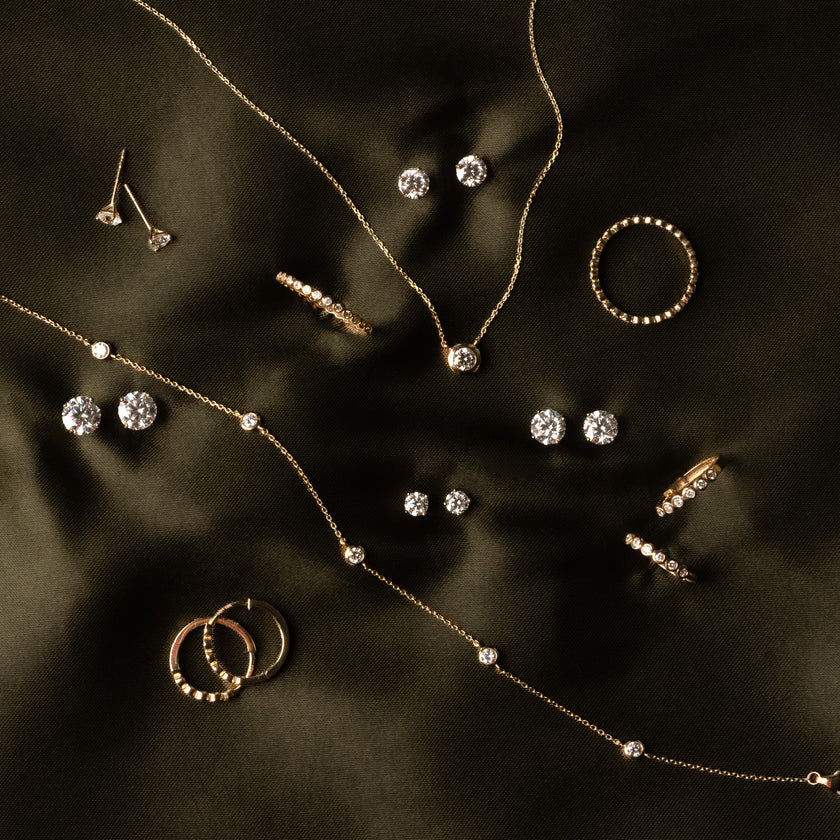 Pieces of gold jewelry with clear gemstones laying on a dark green satin background.