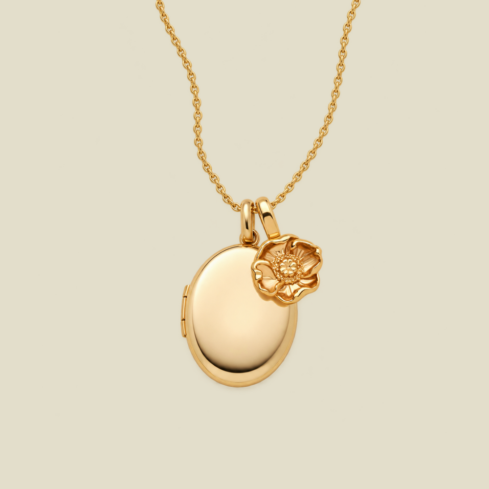 A gold locket necklace with a small poppy flower charm, displayed on a light beige background.