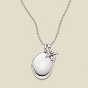 A silver locket necklace with a polished oval pendant and a small holly leaf charm, displayed on a light beige background.