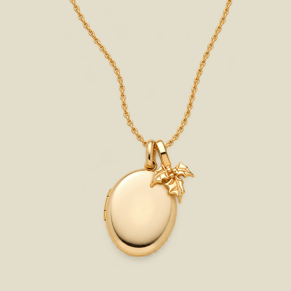 A gold oval locket necklace with a small holly leaf charm, shown on a light beige background.