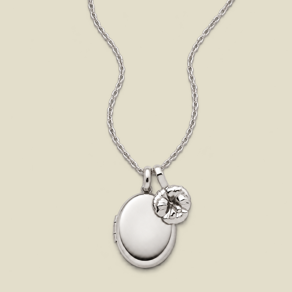 A silver locket necklace with an oval locket and a small violet flower charm, displayed on a light beige background.