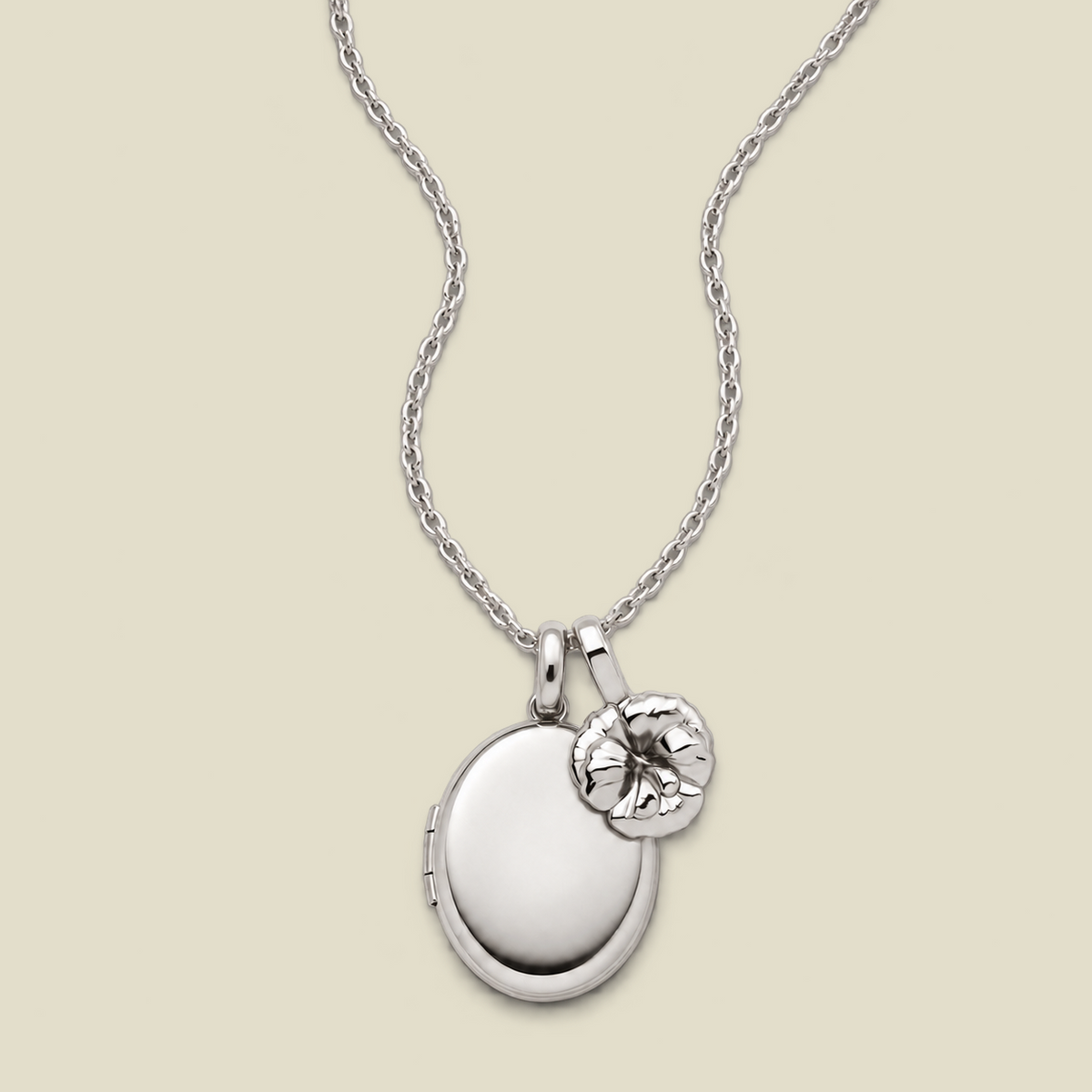 A silver locket necklace with an oval locket and a small violet flower charm, displayed on a light beige background.