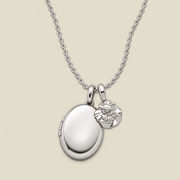 A silver locket necklace with an oval locket and a small carnation flower charm, displayed on a light beige background.