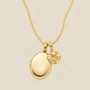 A polished gold locket necklace with an oval locket and a small carnation flower charm, displayed on a light beige background.