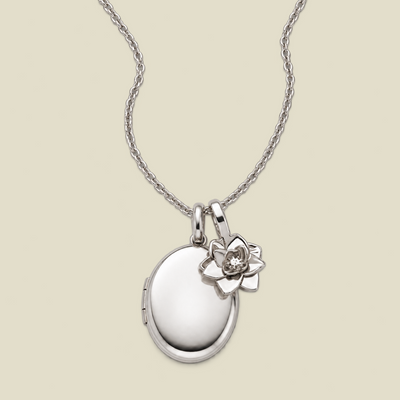 A silver locket necklace with a small lotus flower charm, displayed on a light beige background.