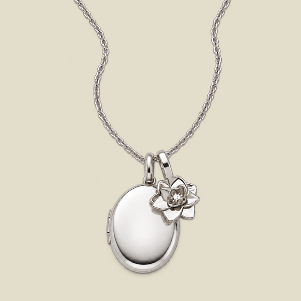 A silver locket necklace with a small lotus flower charm, displayed on a light beige background.