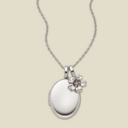 A silver oval locket necklace with a small cherry blossom flower charm, displayed on a light beige background.