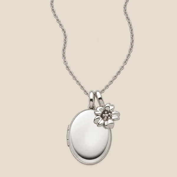 A silver oval locket necklace with a small cherry blossom flower charm, displayed on a light beige background.