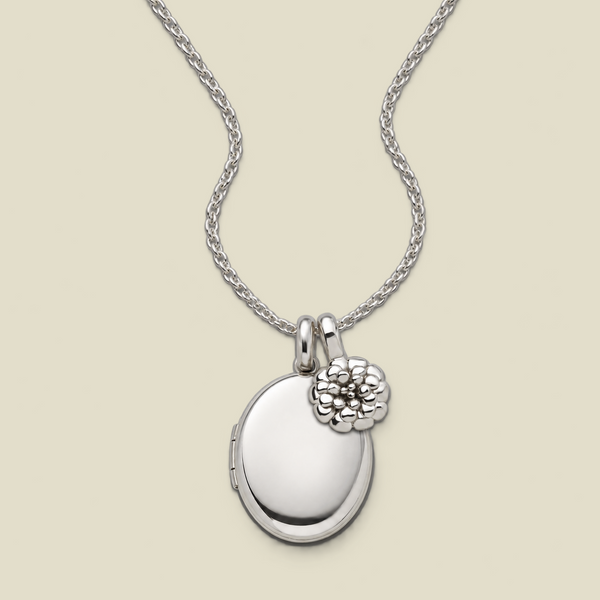 A silver locket necklace with an oval locket pendant and a small textured marigold flower charm, displayed on a light beige background.