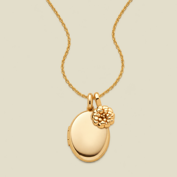A gold locket necklace featuring a polished oval locket pendant with a textured floral charm, suspended from a delicate gold chain against a solid light beige background.