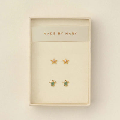 Set of gold stud earrings, one a starfish with a pearl in the center and the other a turtle with a green stone, in a 'Made by Mary' box on a beige background