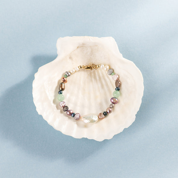 Multi-colored pearl bracelet on a seashell against a light blue background