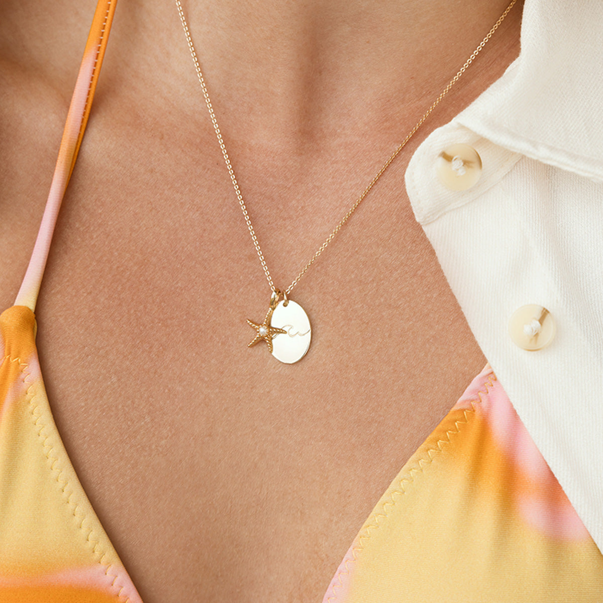 Dainty gold chain necklace with starfish pendant and a large round disc pendant,  worn by a person in an orange and yellow outfit.