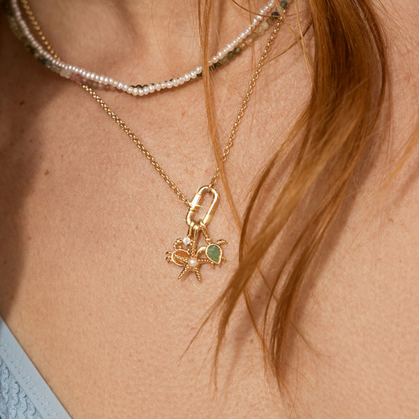 Close-up of a gold necklace with a turtle charm, starfish charm, and crab charm worn by a person with red hair.