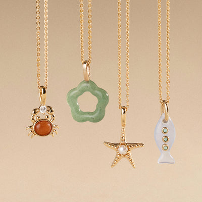 Four gold necklaces with various pendants on a beige background