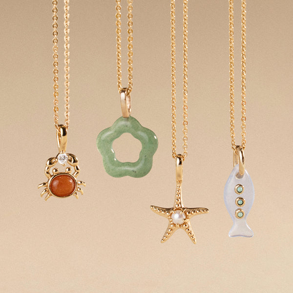 Four gold necklaces with various shaped and colored pendants on a beige background