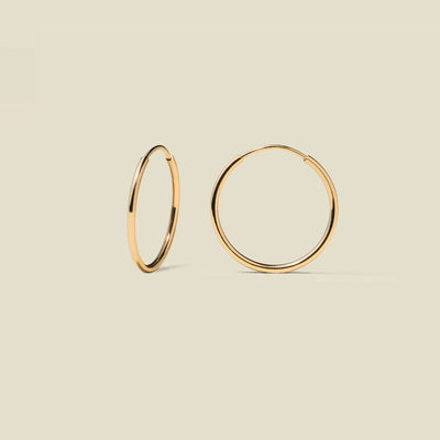 Thin gold hoop earrings on a beige background