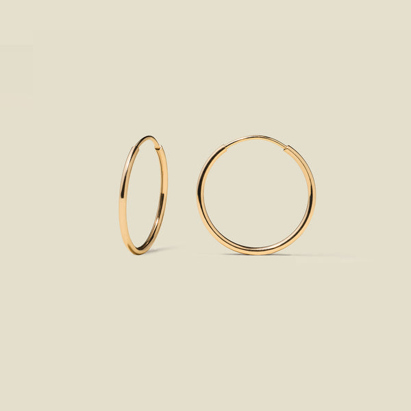 Thin gold hoop earrings on a beige background