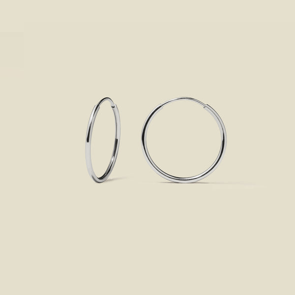 Thin silver hoop earrings on a beige background