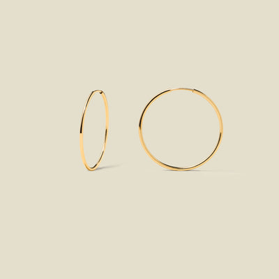 Thin gold hoop earrings on a beige background