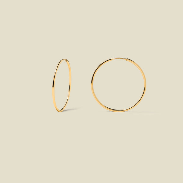 Thin gold hoop earrings on a beige background