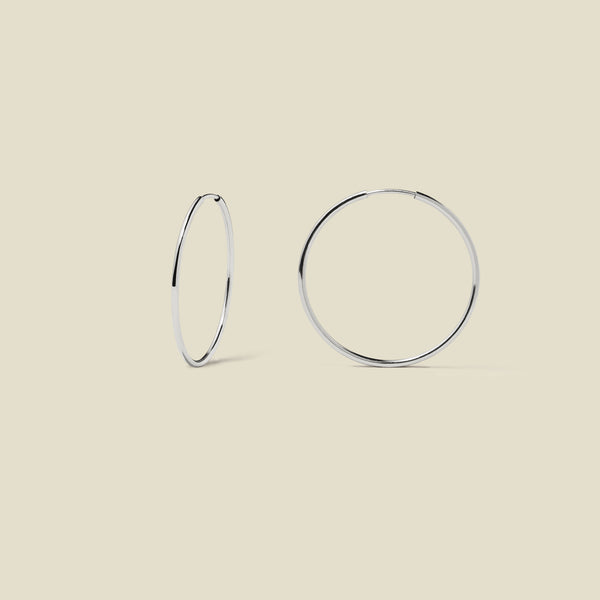 Thin silver hoop earrings on a beige background