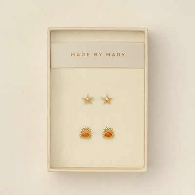 A pair of gold starfish stud earrings with pearls in the center, and a pair of gold crab stud earrings with amber-orange centers and clear crystals, presented in a cream-colored jewelry box with 'MADE BY MARY' printed on the inside header.
