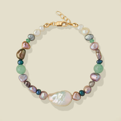 A beaded bracelet featuring a large baroque pearl, and smaller multi-color iridescent pearls, accented with a gold clasp on a light beige background.