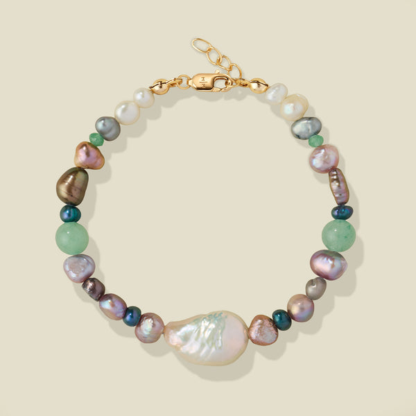 A beaded bracelet featuring a large baroque pearl, and smaller multi-color iridescent pearls, accented with a gold clasp on a light beige background.