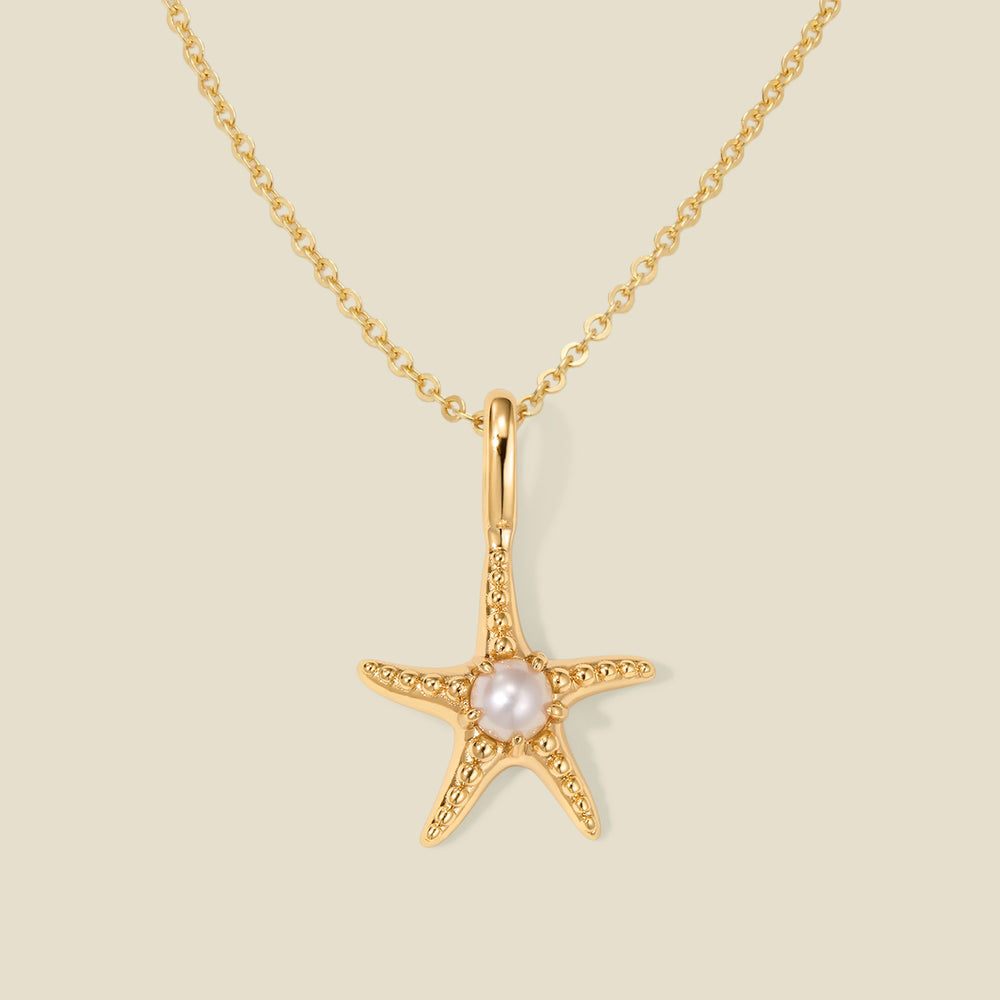 A dainty gold starfish pendant necklace with a central white pearl, displayed on a light beige background.