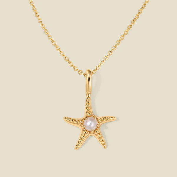 A dainty gold starfish pendant necklace with a central white pearl, displayed on a light beige background.