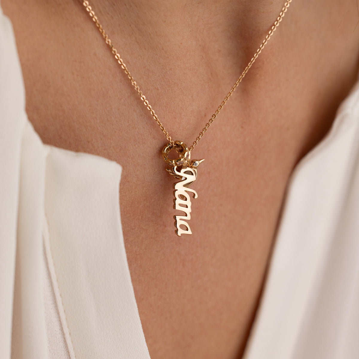Gold necklace with 'Nana' pendant on a person wearing a white top.