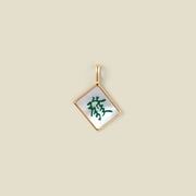 A square diamond-shaped mahjong tile pendant with a gold-tone border and a white inlay featuring a green Chinese character, shown on a solid beige background.