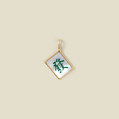 A square diamond-shaped mahjong tile pendant with a gold-tone border and a white inlay featuring a green Chinese character, shown on a solid beige background.