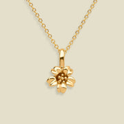 A gold cherry blossom flower pendant necklace on a delicate gold chain, set against a solid light beige background.