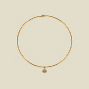 A delicate gold wire circle necklace with a small oval blue stone pendant, displayed on a solid light beige background.