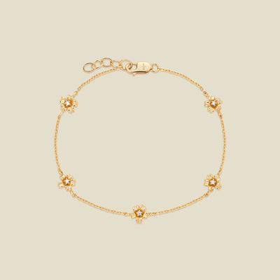 A delicate gold chain bracelet featuring five ornate, textured gold cherry blossom charms with small clear stones, arranged in a circle on a light beige background.