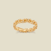 A gold floral-etched ring band with textured cherry blossom flowers and small clear gemstones, shown on a plain warm beige background. 