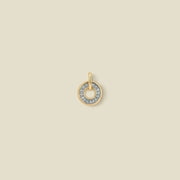 A gold circular pendant featuring light blue baguette-cut stones around a hollow center, displayed against a solid light beige background.