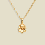 A polished yellow gold necklace with a small lily of the valley flower-shaped pendant, displayed against a solid light beige background.