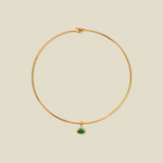 A delicate gold wire necklace with a small oval green gemstone pendant, displayed on a solid light beige background.