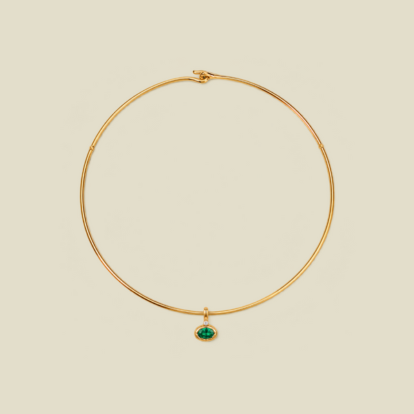A delicate gold wire necklace with a small oval green gemstone pendant, displayed on a solid light beige background.
