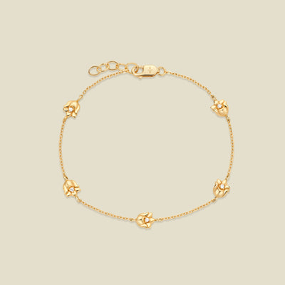 A delicate gold chain bracelet featuring five ornate, textured gold lily of the valley charms with small clear stones, arranged in a circle on a light beige background.