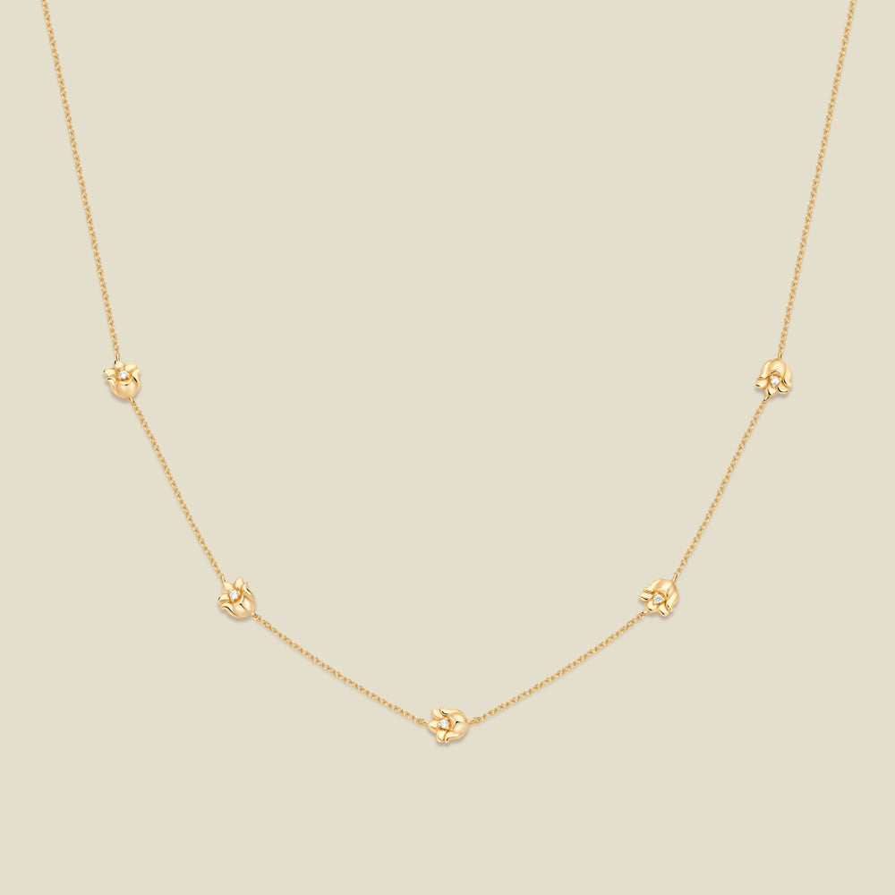 A delicate gold chain necklace featuring five small, evenly spaced textured lily of the valley flower motifs set with tiny clear stones, displayed on a solid light beige background.
