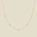 A delicate gold chain necklace featuring five small, evenly spaced textured lily of the valley flower motifs set with tiny clear stones, displayed on a solid light beige background.