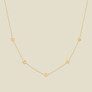 A delicate gold chain necklace featuring five small, evenly spaced textured lily of the valley flower motifs set with tiny clear stones, displayed on a solid light beige background.