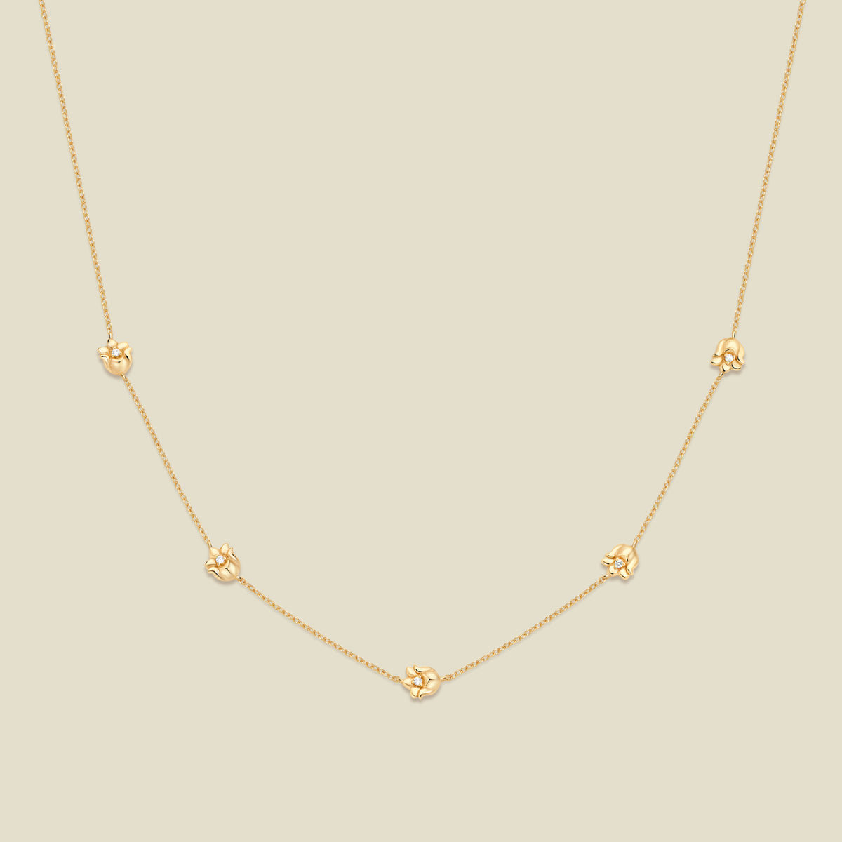 A delicate gold chain necklace featuring five small, evenly spaced textured lily of the valley flower motifs set with tiny clear stones, displayed on a solid light beige background.